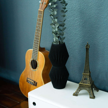 A black matte vase on a white side table next to a guitar and small Eiffel Tower decor. One of Woodland Pulse's black vases.