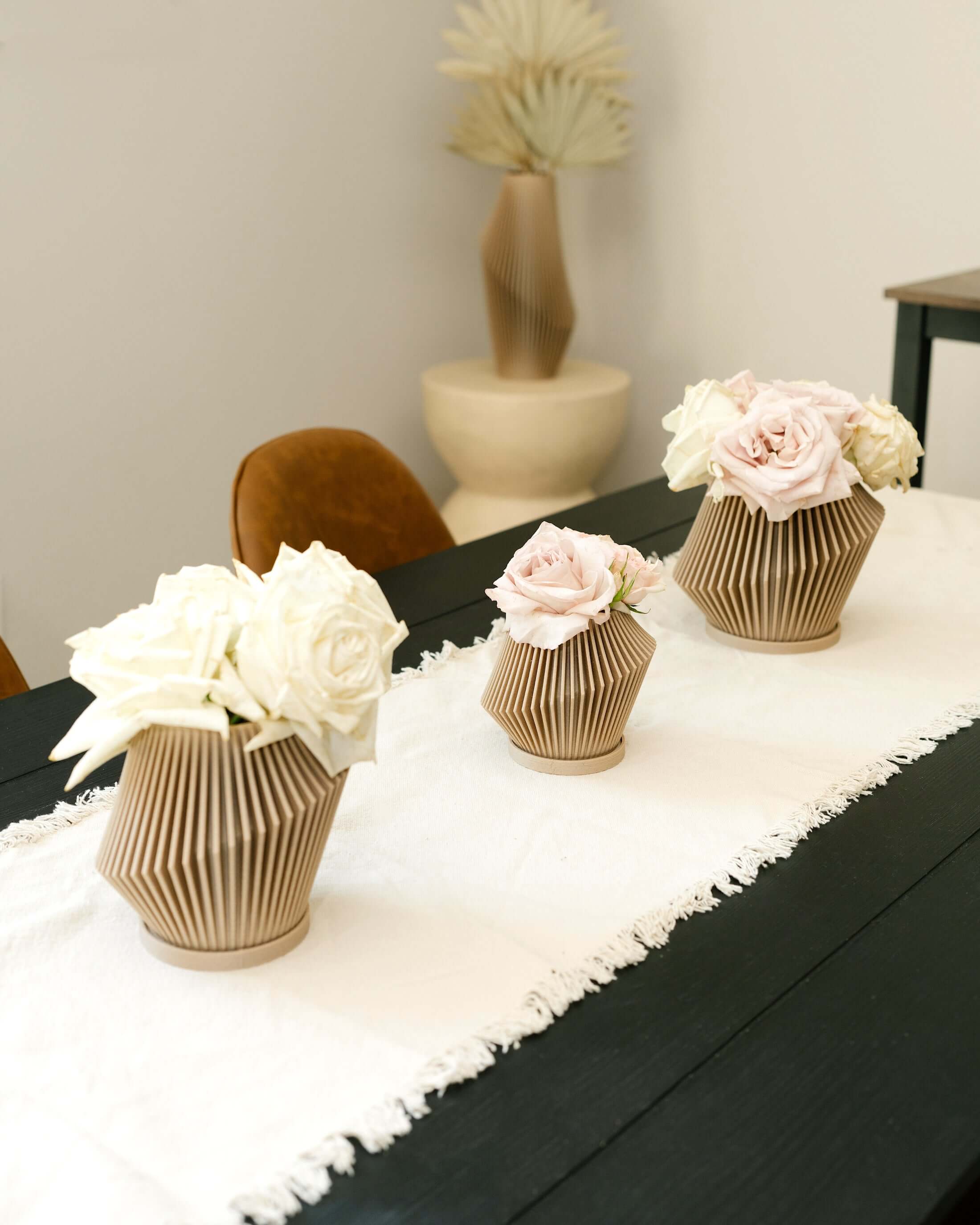 Set of three beige DISC small flowerpots with roses on a white table runner.