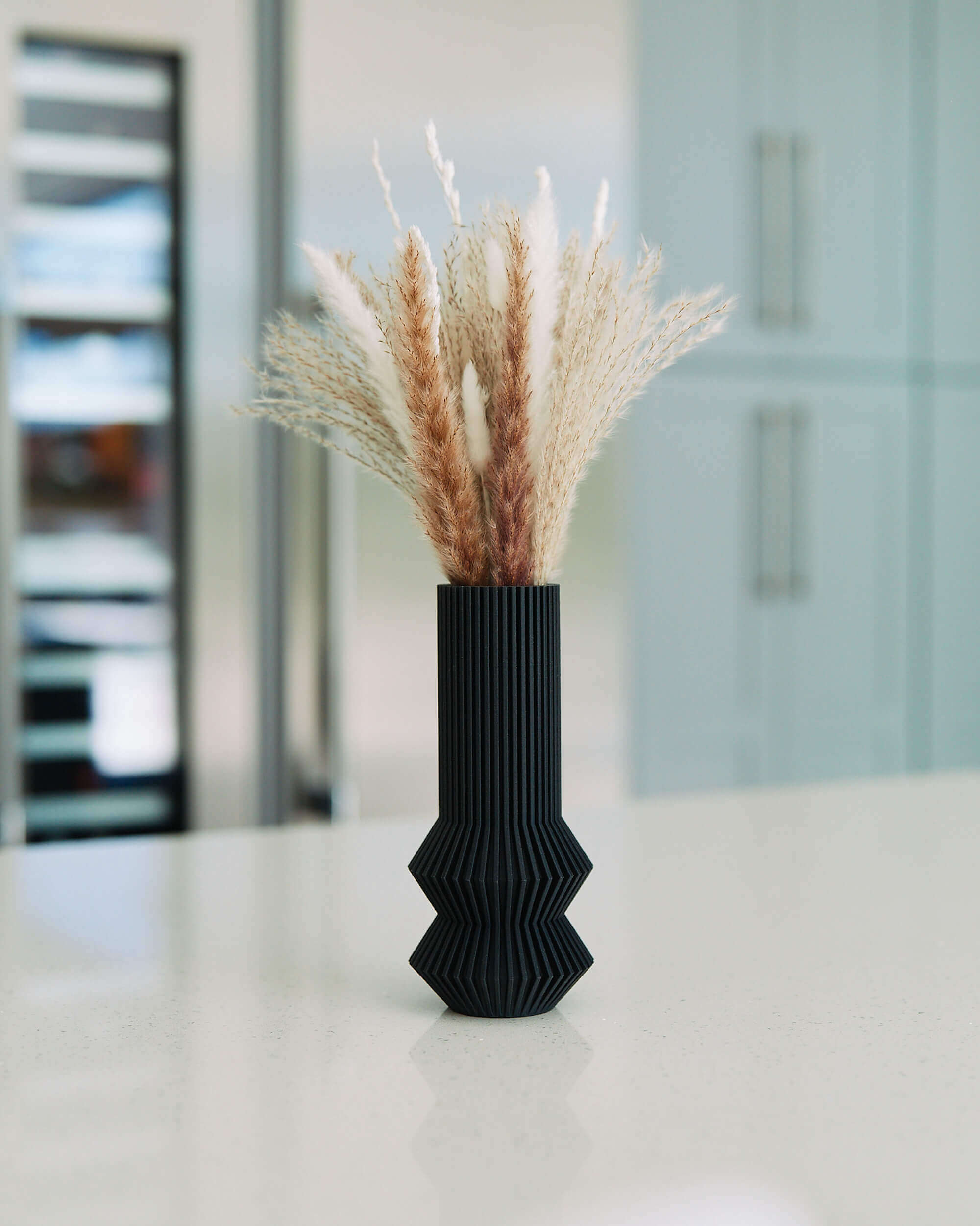 A black matte vase / modernist vase by Woodland Pulse. This is a vase with pampas grass on a white marble countertop.