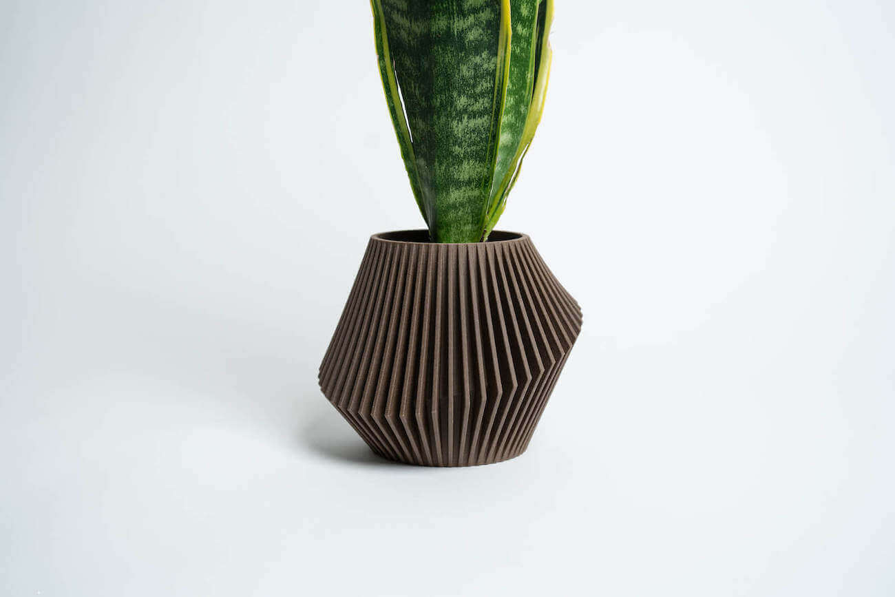 A unique planter, DISC, by Woodland Pulse. This is a brown planter with a snake plant inside.