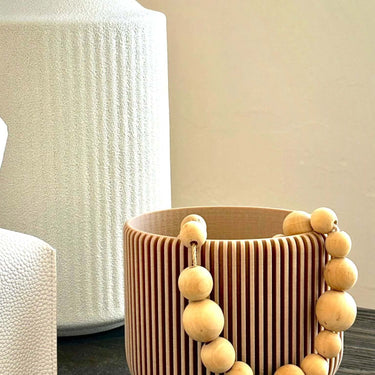 A decor cream pot. This is a beige planter pot with neutral wood chains.