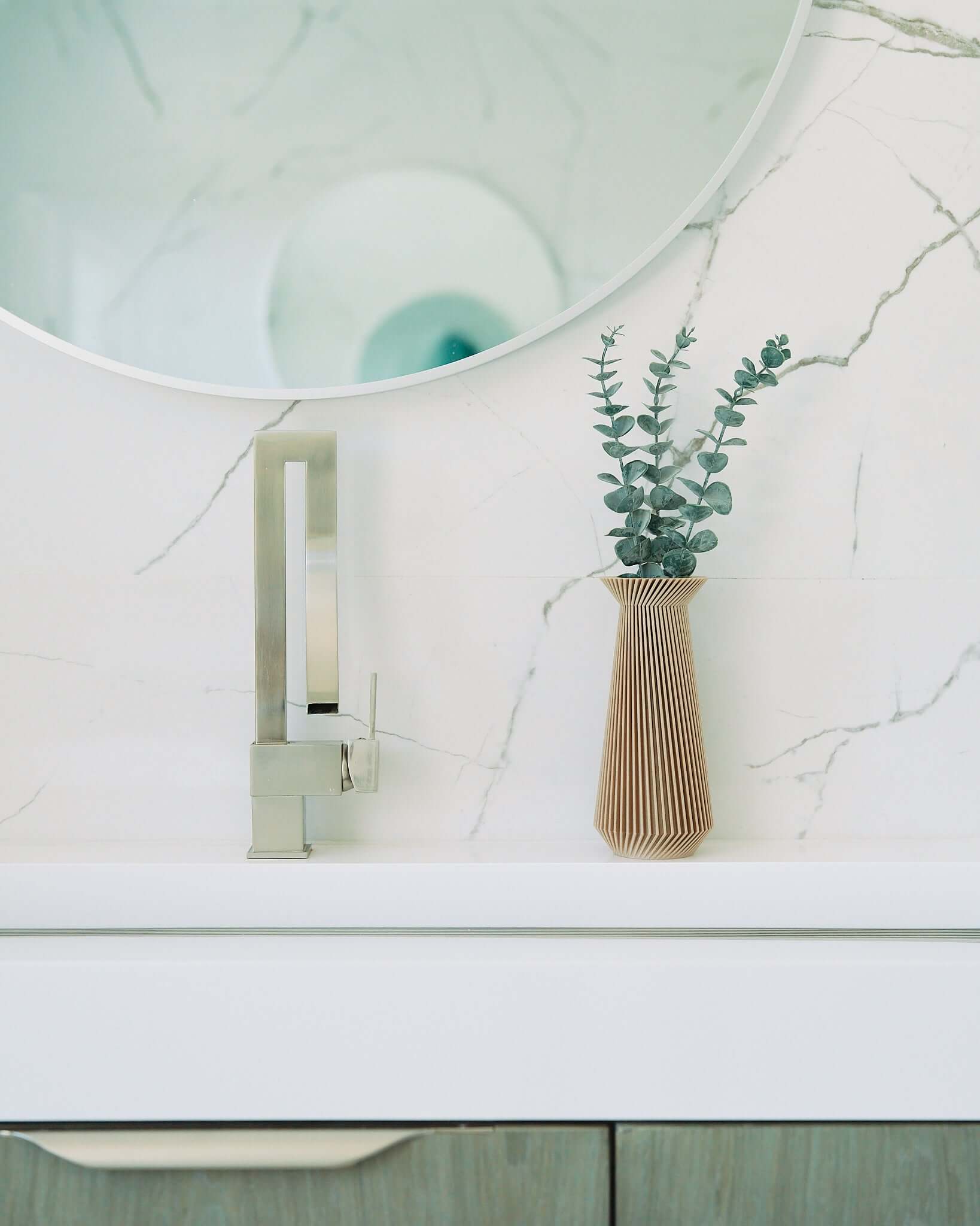 A beige vase / boho vase with eucalyptus on a marble bathroom sink countertop. 