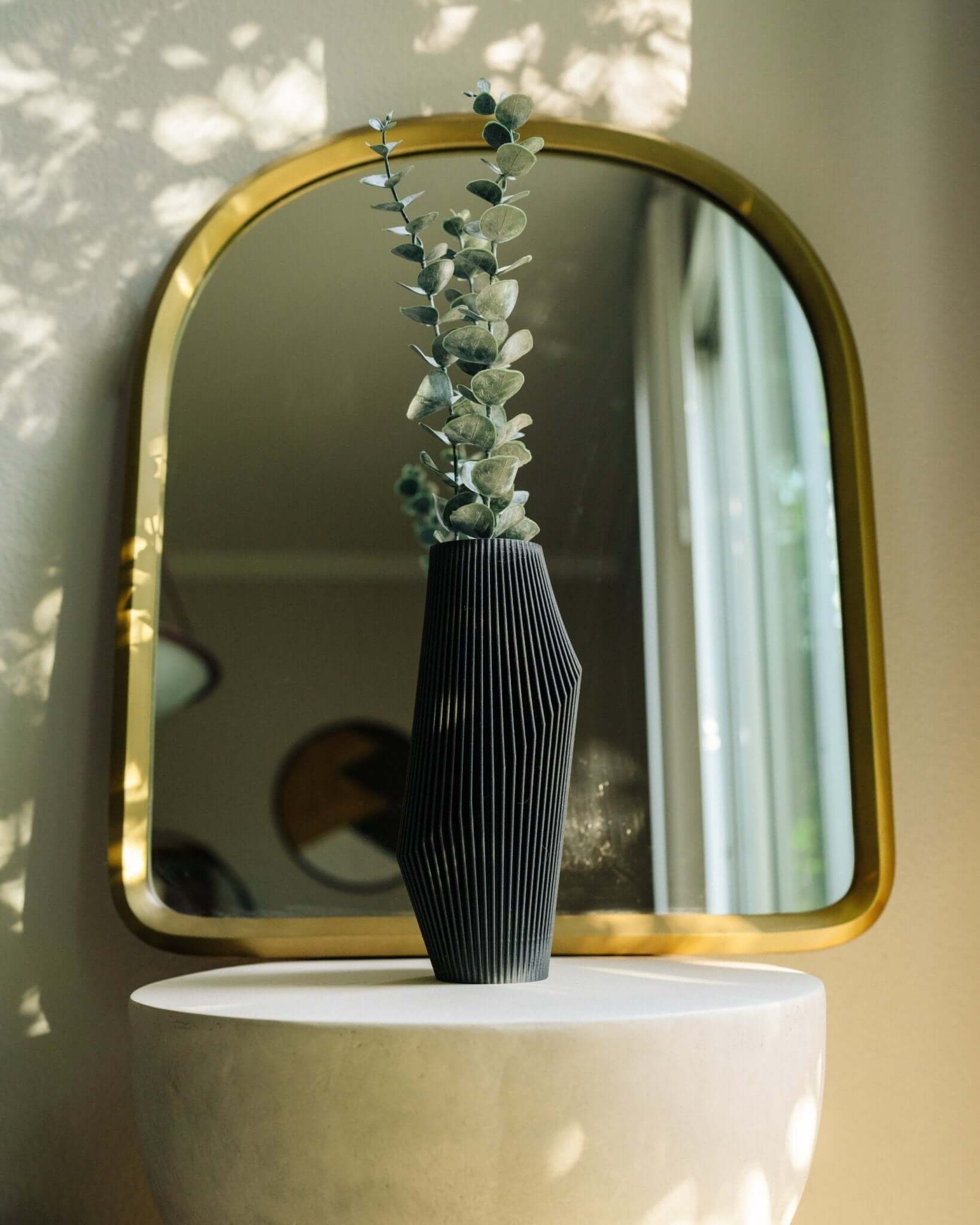 Unique vase with eucalyptus near decorative mirror.