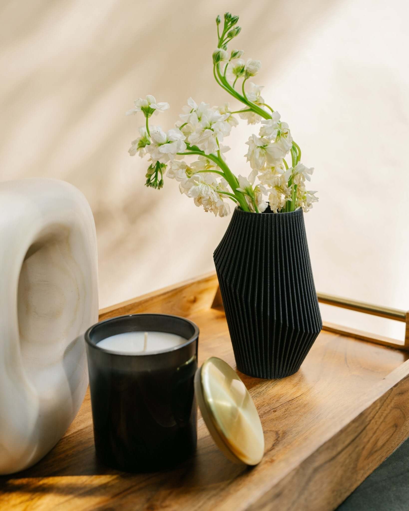 A black small vase with flowers next to a candle.